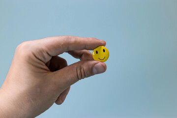 Yellow smiling emoticon in your hand on blue screen