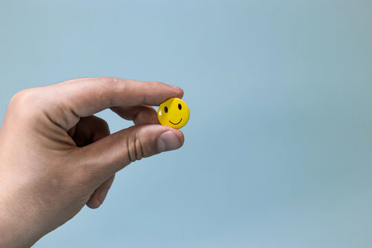 Yellow smiling emoticon in your hand on blue screen