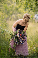Blonde girl with a bouquet of lupines in a field walking in the summer