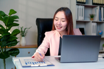 Asian businesswoman working with financial documents using laptop analyzing sales data and economic growth graph chart, business strategy and planning