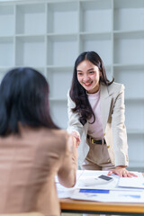 Two asian businesswomen shaking hands after closing a deal over a table with documents and...