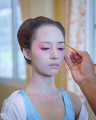 Beautiful Asian female tourist receives traditional Geisha or Maiko makeup, an ancient Japanese culture for beauty by professional make-up artist.