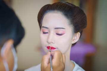 Beautiful Asian female tourist receives traditional Geisha or Maiko makeup, an ancient Japanese culture for beauty by professional make-up artist.