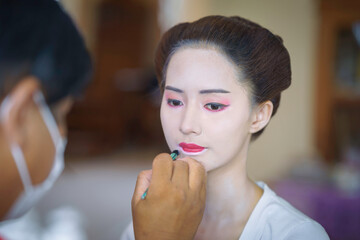 Beautiful Asian female tourist receives traditional Geisha or Maiko makeup, an ancient Japanese culture for beauty by professional make-up artist.