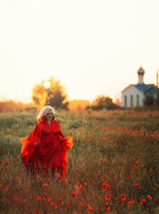 Beautiful girl in a red dress in a poppy field with a big poppy