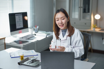 Asian female doctor wearing lab coat holding medicine bottle having video conference with patient...