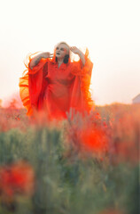 Beautiful girl in a red dress in a poppy field with a big poppy