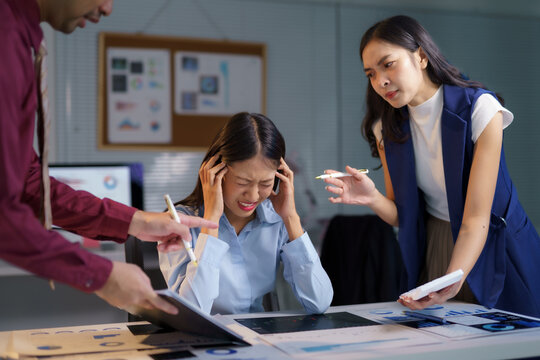 Asian businesspeople arguing with stressed businesswoman having headache during difficult meeting in office at night