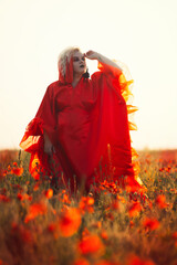 Beautiful girl in a red dress in a poppy field with a big poppy