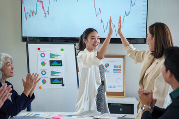 Asian businesswomen high fiving celebrating successful project during an office meeting with colleagues clapping