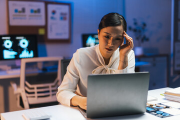 Asian businesswoman working late using laptop having a headache from overwork and stress in office at night