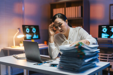 Tired businesswoman looking at documents and having a headache while working late in office at night