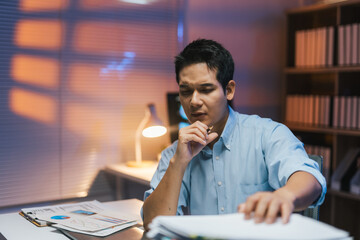 Young professional analyzing paperwork at night, concentrating on business tasks under warm lamp...