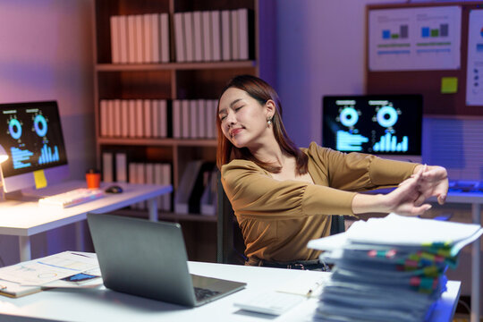 Young office worker stretching and relaxing muscles after long hours at the computer, finding relief from fatigue and stress at her desk
