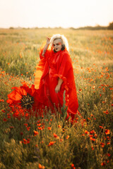 Beautiful girl in a red dress in a poppy field with a big poppy