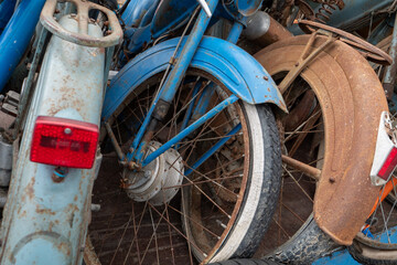 Pile of old motorbikes with one of them having a red tail light. The bikes are stacked on top of each other