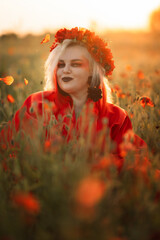 Beautiful girl in a red dress in a poppy field with a big poppy