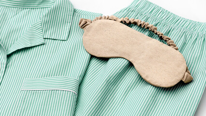 Beige eye mask for sleep on folder striped green pajama, close up texture fabric, minimal lifestyle aesthetic banner. Top view woman sleeping mask for comfort rest, healthy trend, stylish sleepwear