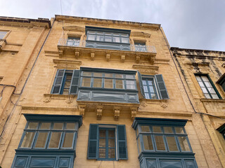 Traditional Maltese facade with blue wooden balconies and shutters on a yellow stone building under...