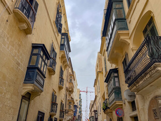 Narrow Maltese street with traditional blue wooden balconies and limestone buildings under a clear sky