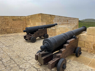 Two historic iron cannons on wooden carriages stand side by side on a stone terrace in a Maltese...