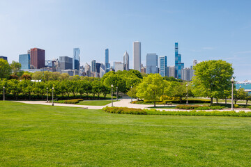 Naklejka premium Sunny view of downtown Chicago with iconic skyscrapers rising above a lush green park meadow