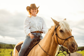 A woman is confidently riding a horse while wearing a cowboy hat