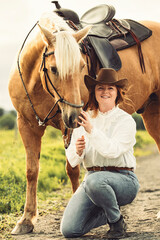 A woman, proudly wearing a cowboy hat, stands next to her horse