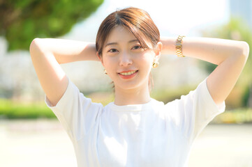 両腕を頭の後ろで組んで爽やかに微笑む女性の明るい昼間のひととき