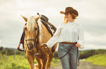 A woman, proudly wearing a cowboy hat, stands next to her horse