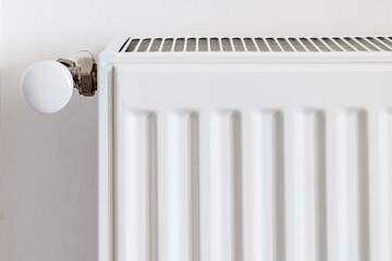 Side view of a white radiator with a round thermostat valve, minimalist interior background, focus on central heating detail and equipment design
