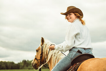 A woman is wearing a cowboy hat while riding a horse in an open field