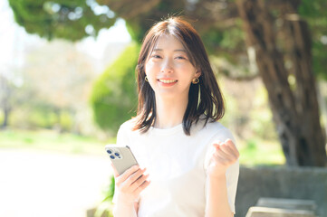 白トップスの女性がスマホを持ってガッツポーズをしながら笑顔を見せる