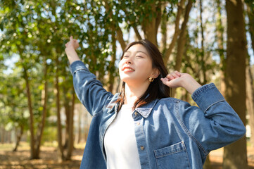 春の森林の中で両手を大きく開き明るい笑顔を見せる女性の開放的な姿