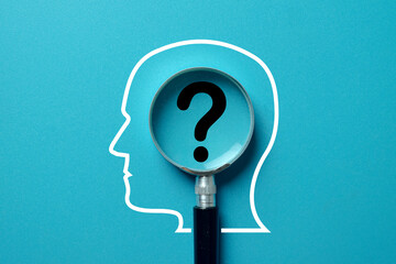 A magnifying glass focusing on a question mark inside a human head outline. Concept for psychology,...