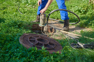 pumping out sewage with a drainage pump, man pumps out sewage from a cesspool in the backyard,...