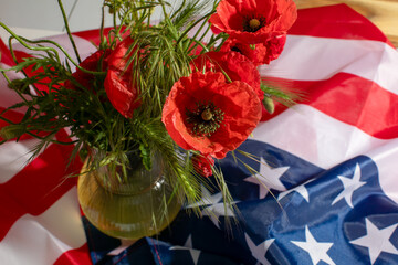 Brilliant red poppies dance on a vase against the bold tapestry of the American flag, echoing...