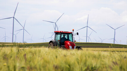 Red tractor meandering through verdant field under stoic wind turbines, celebrating Earth Day and National Agriculture Week symbiosis