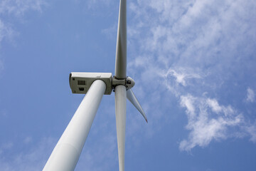 Giant wind turbine slicing azure sky amidst drifting clouds, embodying Earth Day's renewable energy...