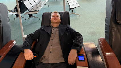 Reclined in a tranquil airport massage chair, a Caucasian man dreams unwindingly before boarding,...