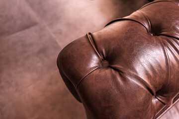 Close-up of brown leather chesterfield sofa armrest. The natural creases of showcasing the quality and luxury of classic interior furniture design. Selective focus.