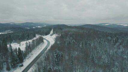 Aerial view of a winding snowy mountain road cutting through a dense winter forest. Mountain road...