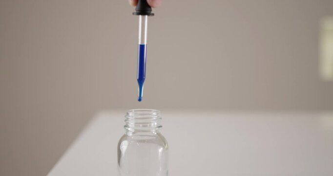 Sample drops of blue ink are filled into a small glass by scientists with a pipette in a laboratory