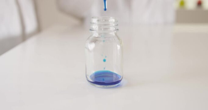 Sample drops of blue ink are poured into a small glass by scientists with a pipette in a laboratory