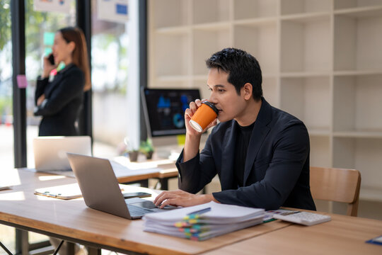 A man is sitting at a desk with a laptop and a cup of coffee