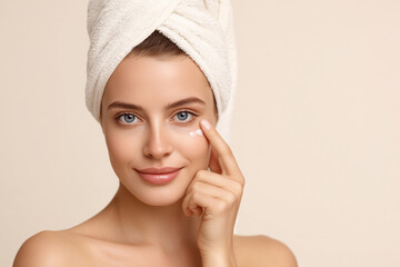 High-resolution portrait of young woman applying under-eye cream with gentle smile