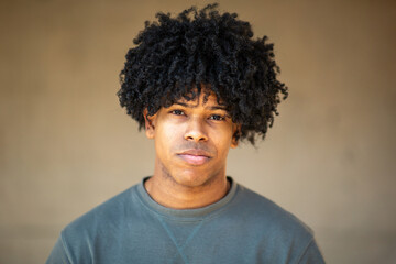 Confident Latin young man with curly hair posing with a smirk against neutral background