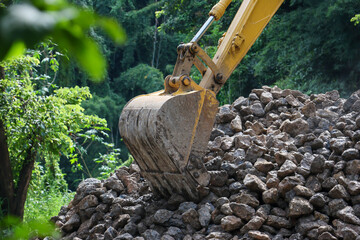 A backhoe is scooping up a large pile of rocks to build a road barrier.