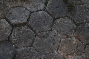 Hexagonal concrete pavement with interspersed weeds in an outdoor area