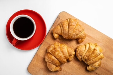 Freshly baked croissant on a wooden tray and a cup of coffee with a white background. Top view